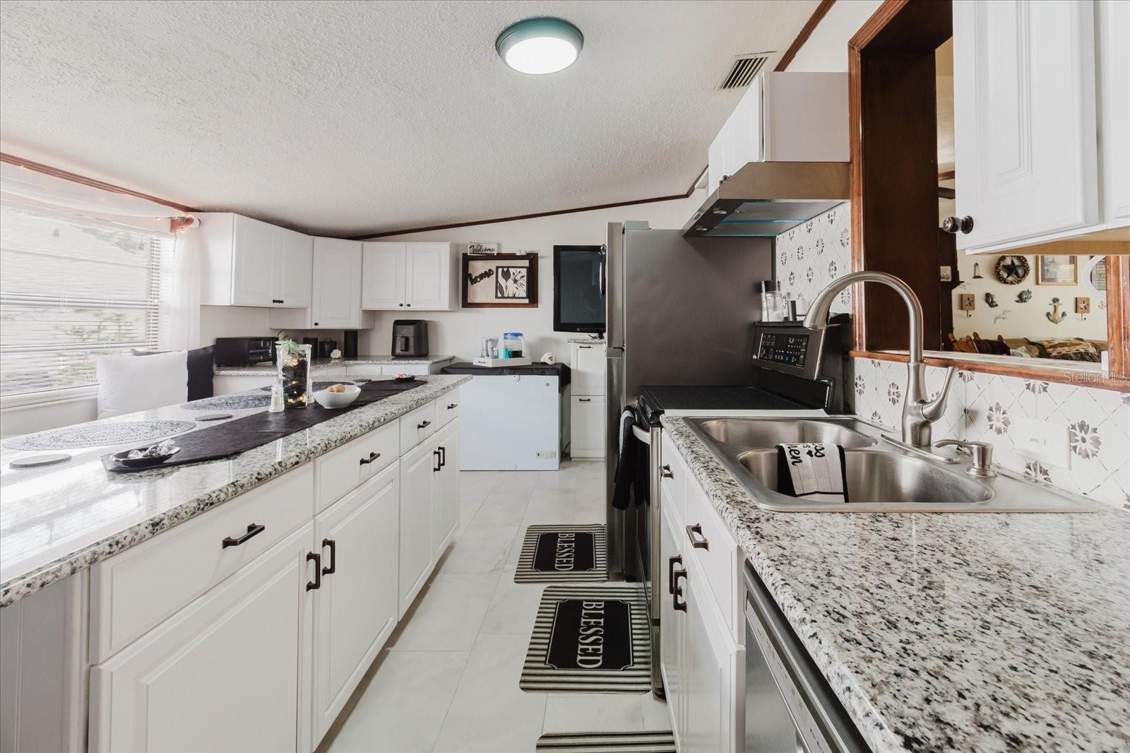 Updated Kitchen With Granite Counters, Stainless Steel Appliances, & Marble Looking Floor Tile. Seating For 4 People At Kitchen Island. Doorway Leads To Backyard and The Laundry Closet. All Kitchen Appliances Stay.