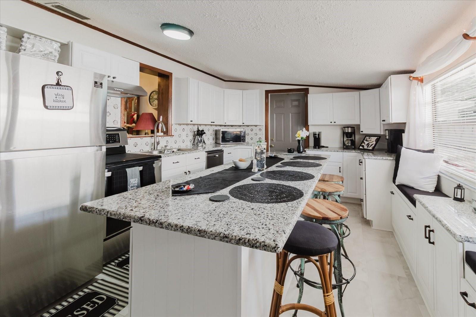 Updated Kitchen With Granite Counters, Stainless Steel Appliances, & Marble Looking Floor Tile. Seating For 4 People At Kitchen Island. Doorway Leads To Backyard and The Laundry Closet. All Kitchen Appliances Stay.