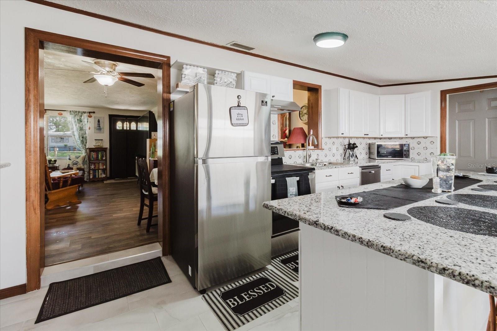 Updated Kitchen With Granite Counters, Stainless Steel Appliances, & Marble Looking Floor Tile. Seating For 4 People At Kitchen Island. Doorway Leads To Backyard and The Laundry Closet. All Kitchen Appliances Stay. Doorway On Right Leads To Backyard.