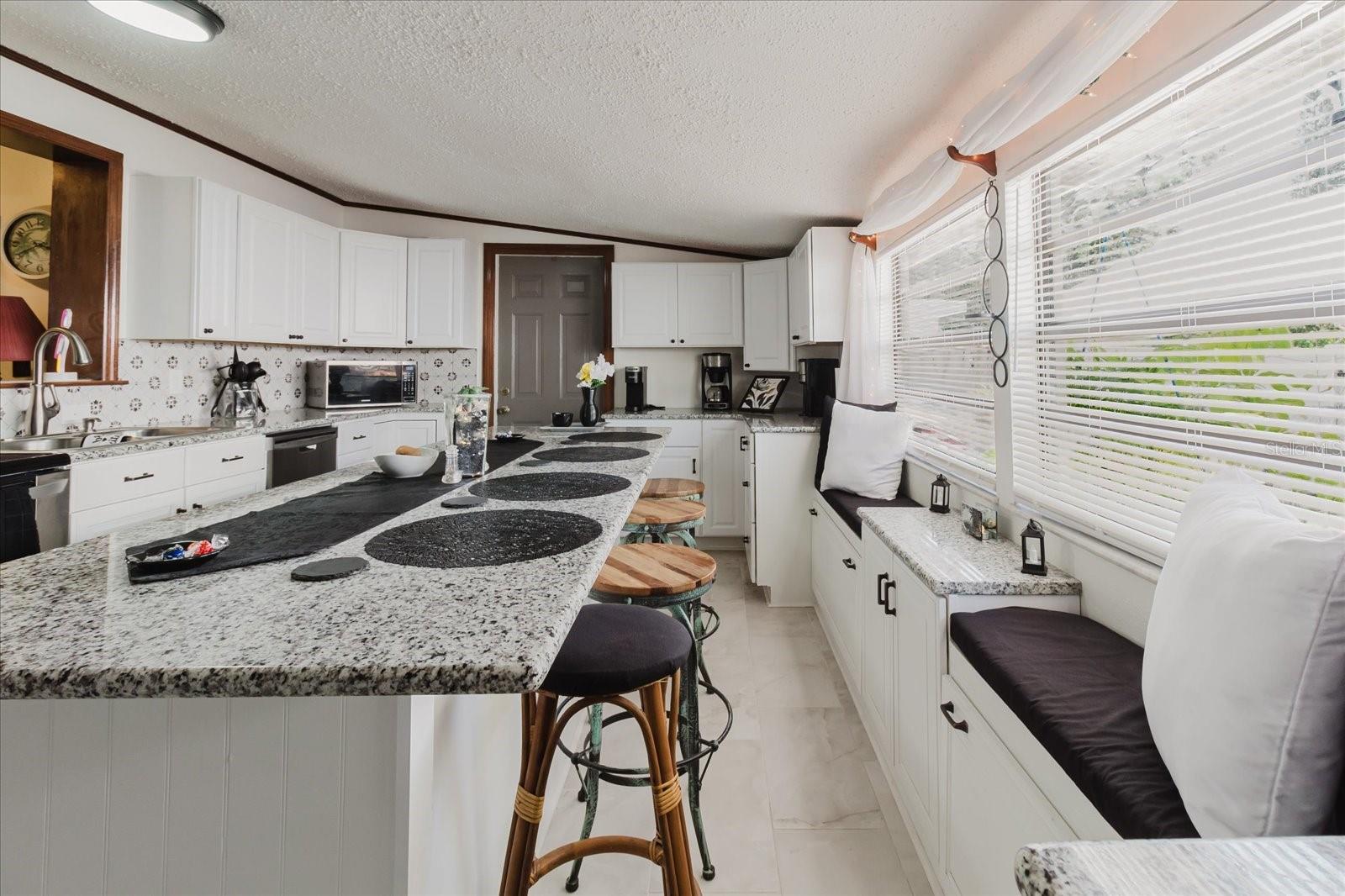 Updated Kitchen With Granite Counters, Stainless Steel Appliances, & Marble Looking Floor Tile. Seating For 4 People At Kitchen island. Doorway Leads To Backyard and The Laundry Closet. All Kitchen Appliances Stay. Doorway Leads To Backyard. Passthru Goes To The Dining Area