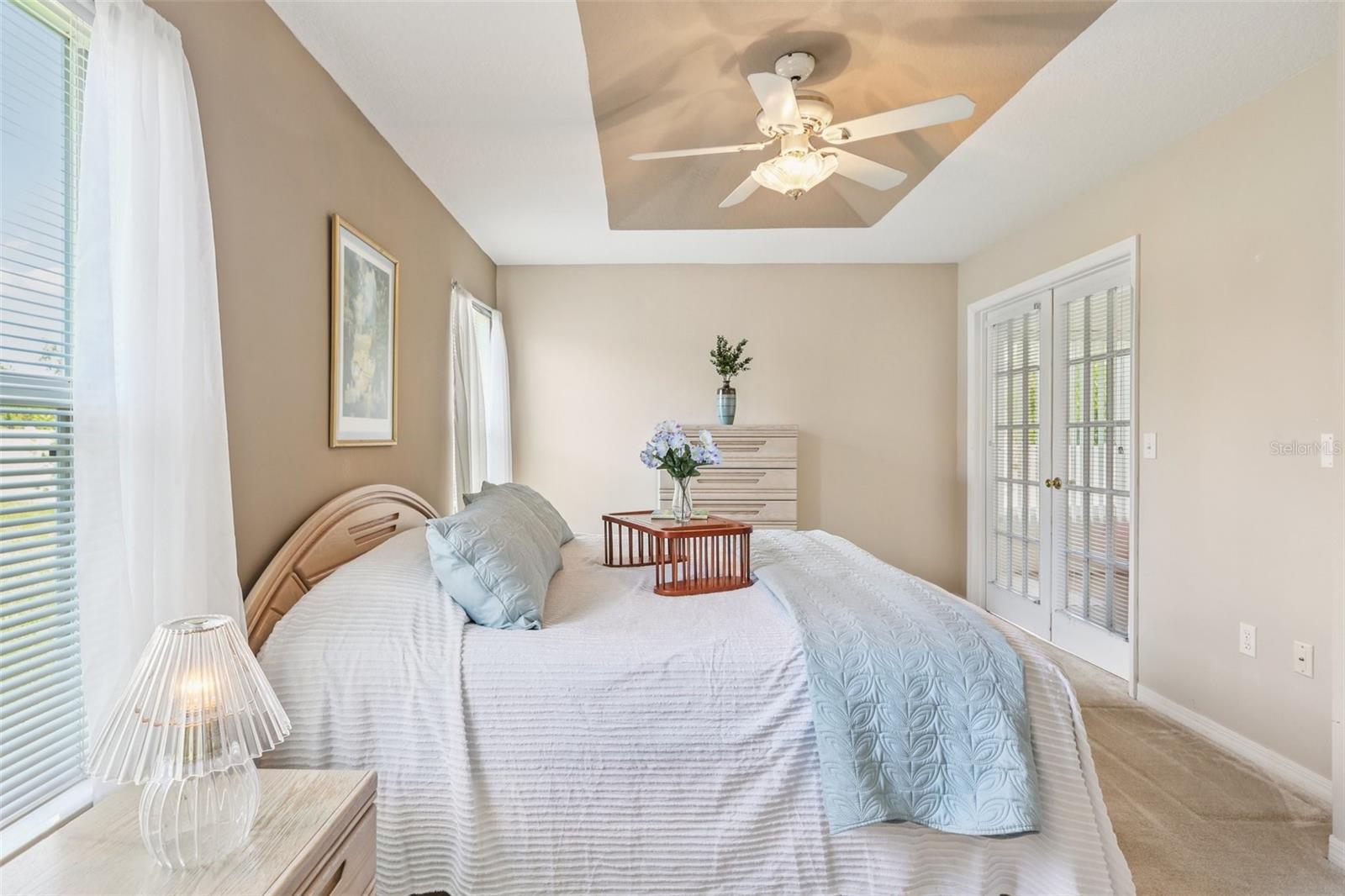 Primary bedroom tray ceiling and ceiling fan. French doors lead to screened lanai.