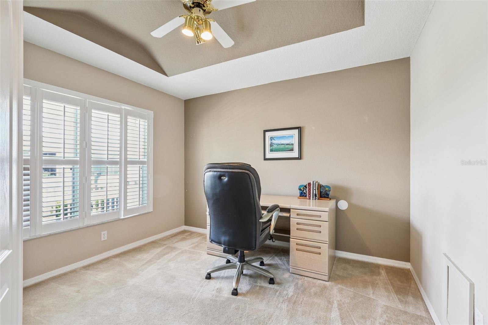 Office/hobby room in front of home features tray ceiling, ceiling fan and plantation shutters.