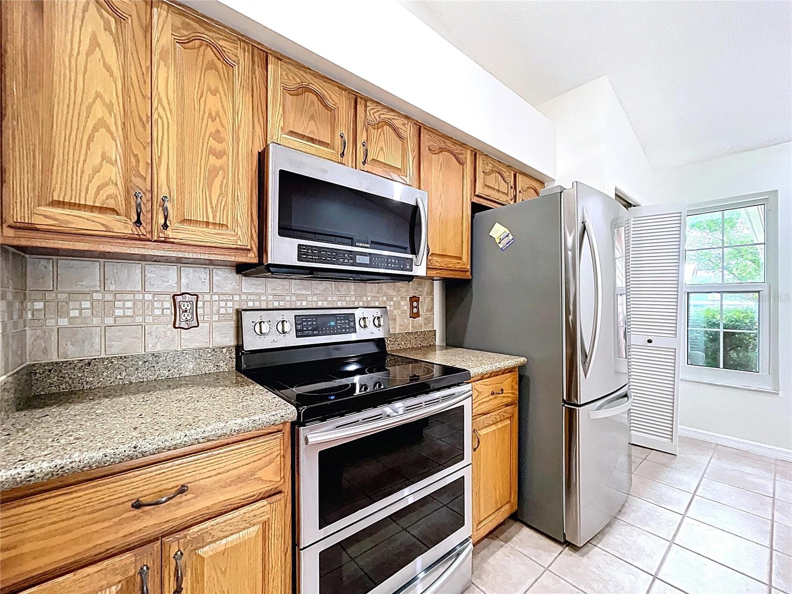 Designed for function and flow, the kitchen features a vaulted ceiling, a center island, and stainless steel Samsung appliances—including a flex double oven.