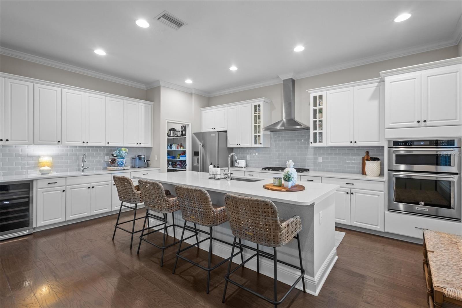 Kitchen features center island, quartz countertops, walk in pantry, gas stovetop, and wet bar area with beverage fridge