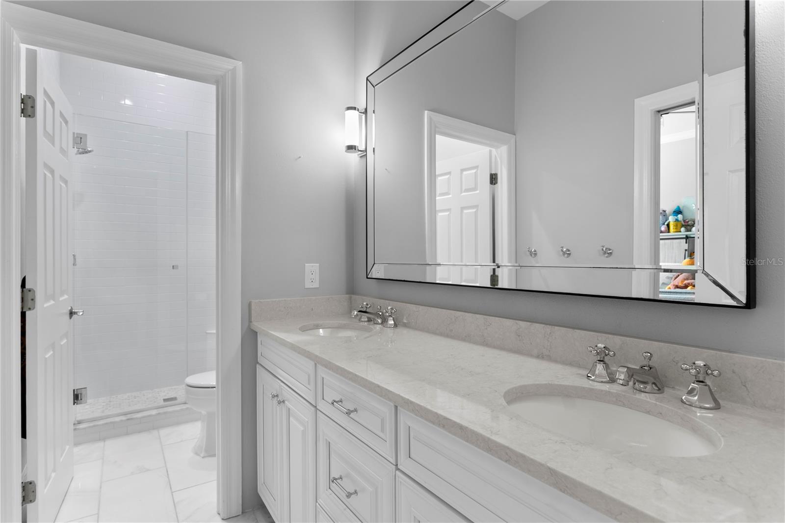 The hallway bathroom offers double vanities and a shower equipped with shelving, providing ample space to store personal care products