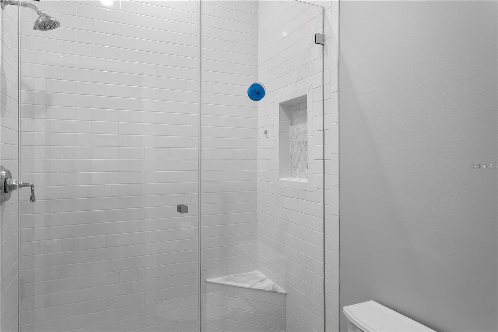 The hallway bathroom offers double vanities and a shower equipped with shelving, providing ample space to store personal care products
