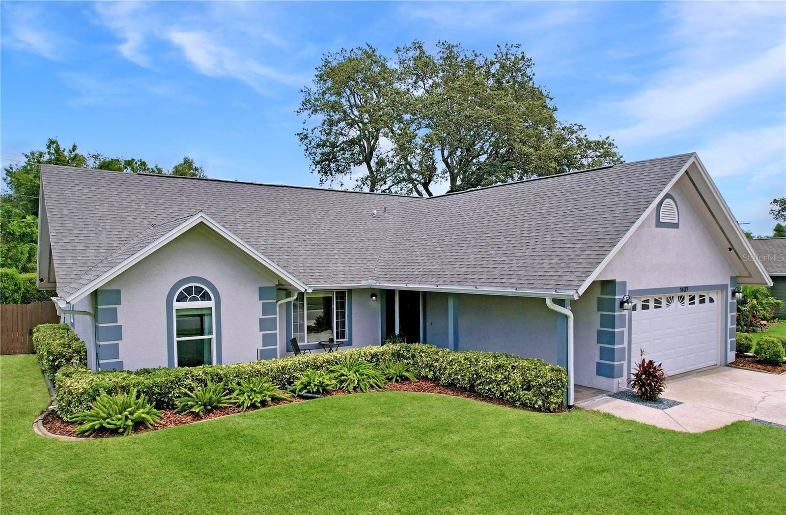 This elevated front yard view showcases the home’s beautiful gables, arched window, and the mature oak tree in back, offering both beauty and shade.