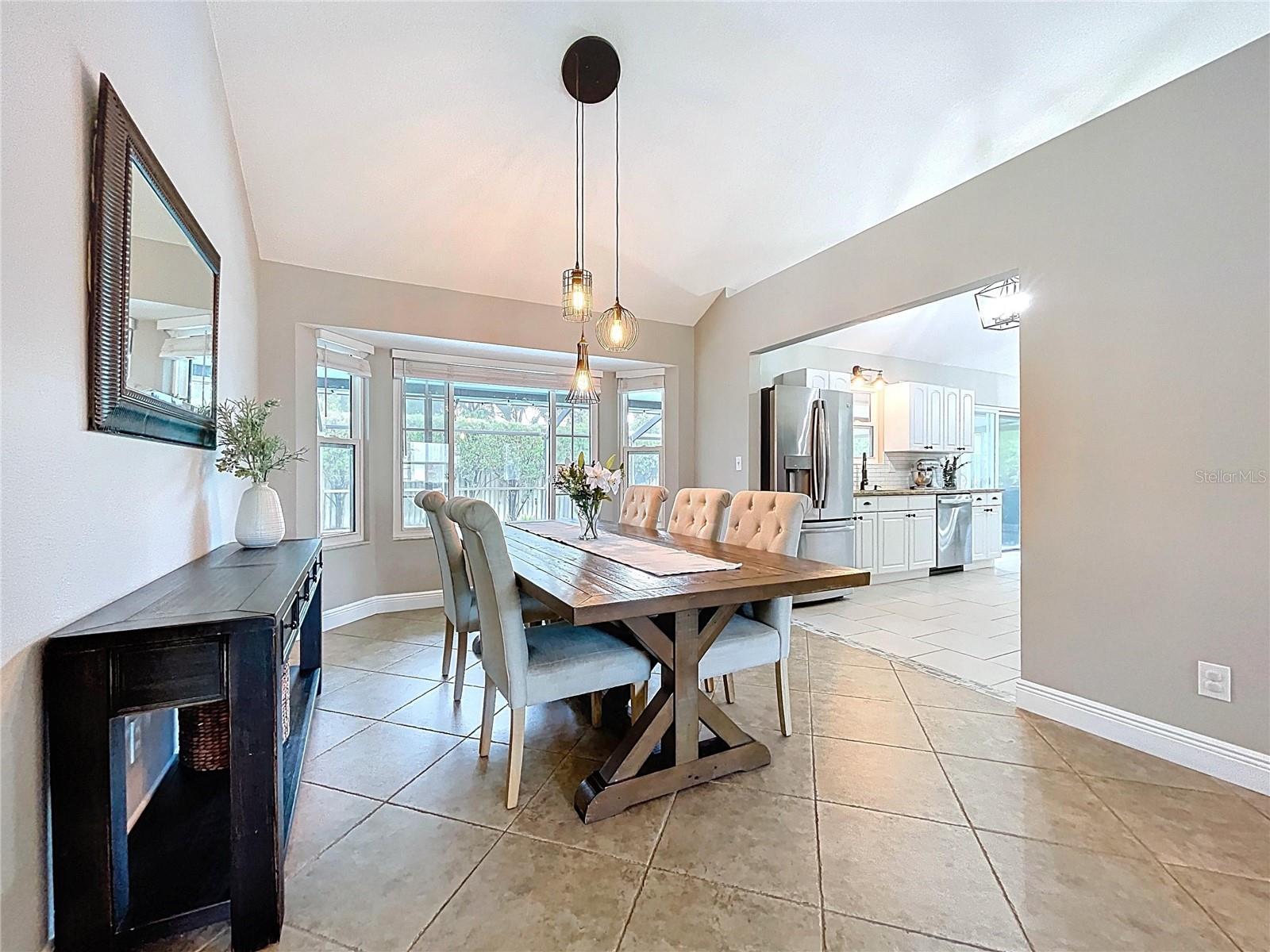 A welcoming perspective that showcases the dining area’s size, pendant lighting, and large windows offering backyard views.
