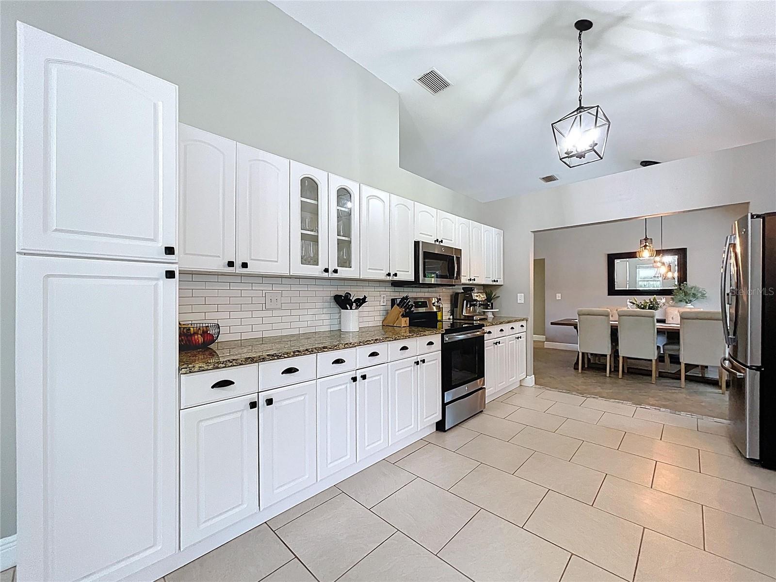 Well-appointed galley-style kitchen with white cabinetry, granite countertops, stainless steel appliances, and subway tile backsplash. Modern lighting and ample storage complete the space.