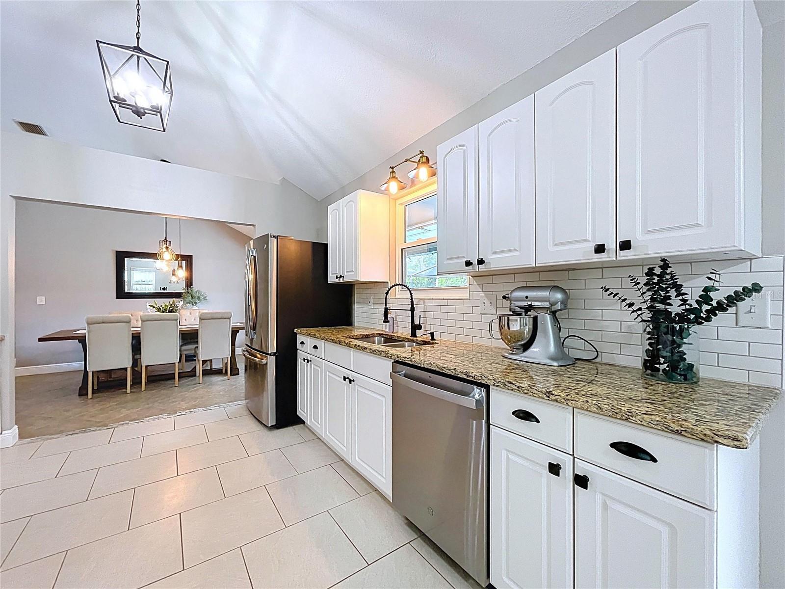 A closer look at the sink-side of the kitchen reveals granite counters, white cabinetry with updated hardware, and a window above the sink for added brightness.