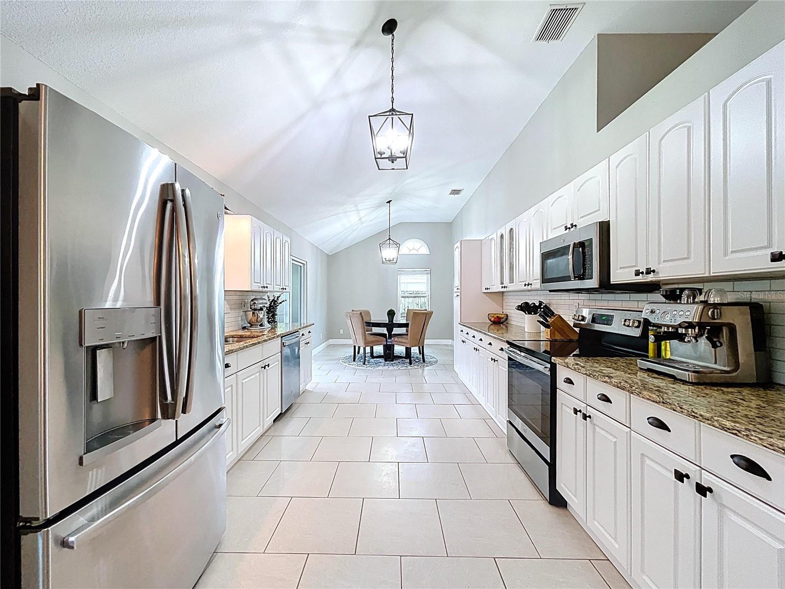 A spacious galley-style kitchen leads seamlessly into the breakfast area, offering abundant storage and stainless steel appliances under vaulted ceilings.