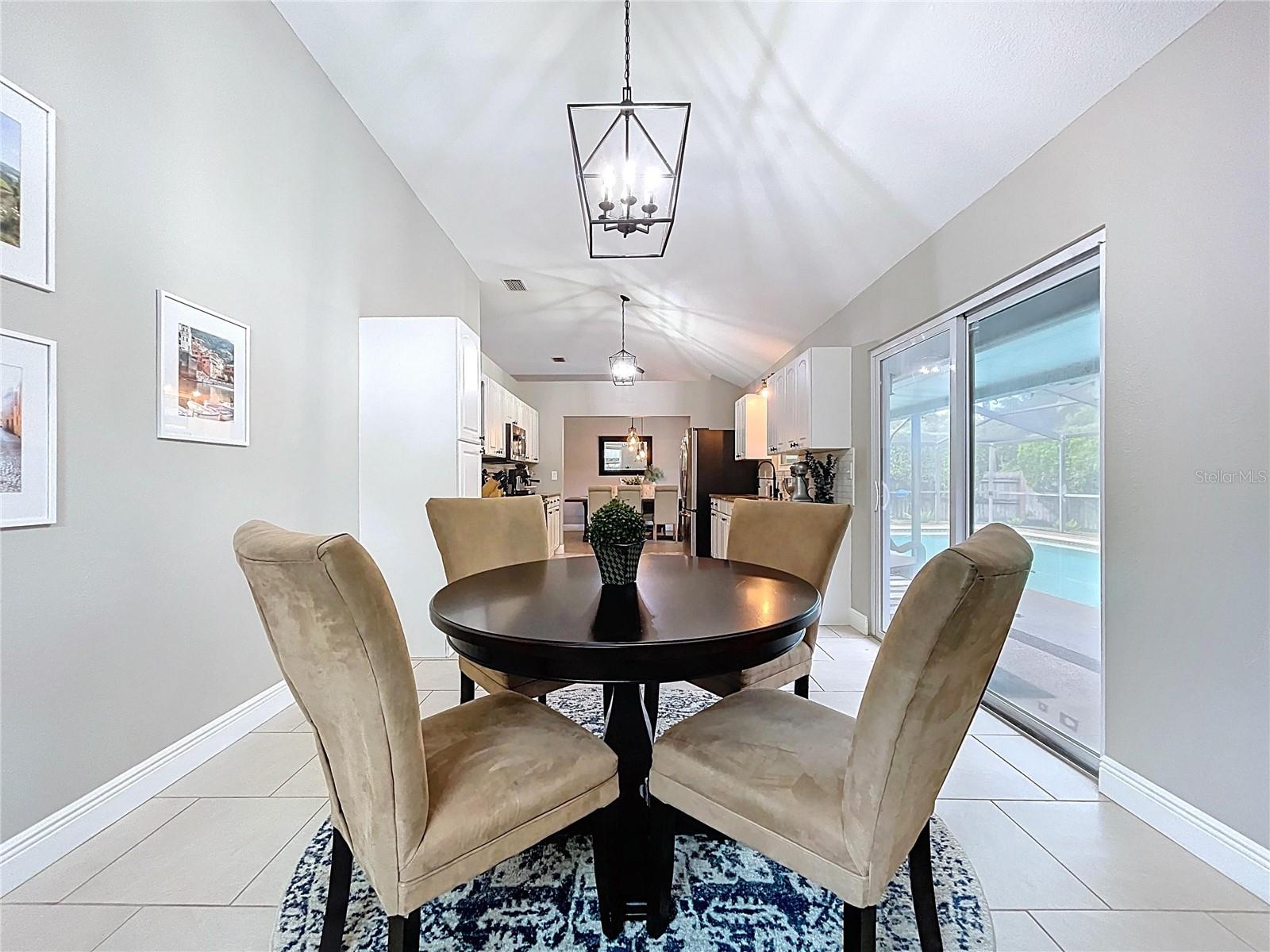 Enjoy relaxed meals in this inviting nook featuring neutral tile, a modern pendant fixture, and access to the screened-in patio beyond.