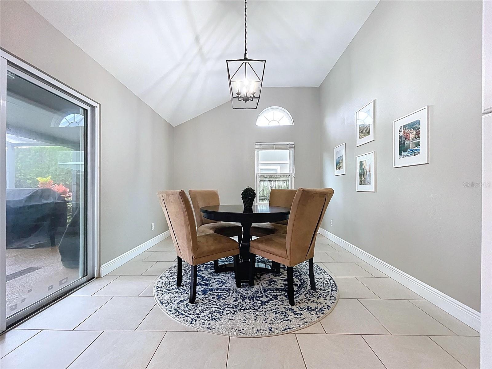 Bright and welcoming nook with vaulted ceiling, arched transom window, and a peaceful backyard view.