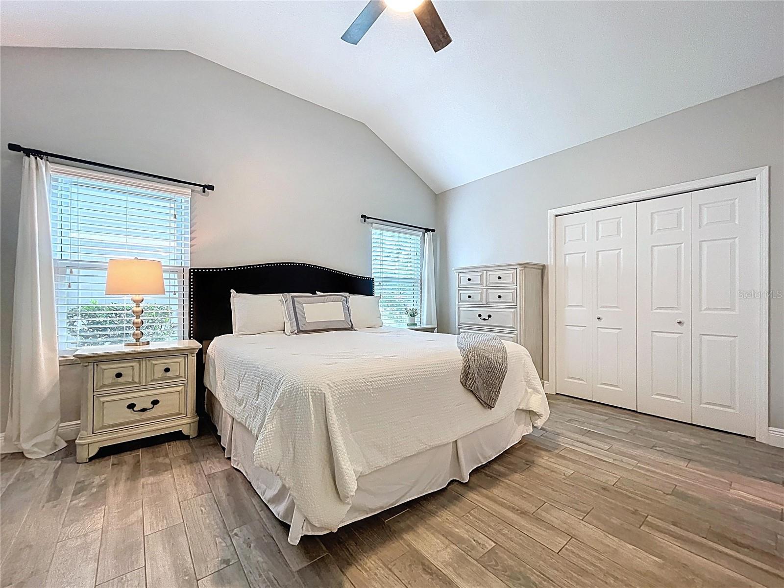 The serene primary suite features vaulted ceilings, wood-look tile flooring, and dual windows that fill the space with natural light.