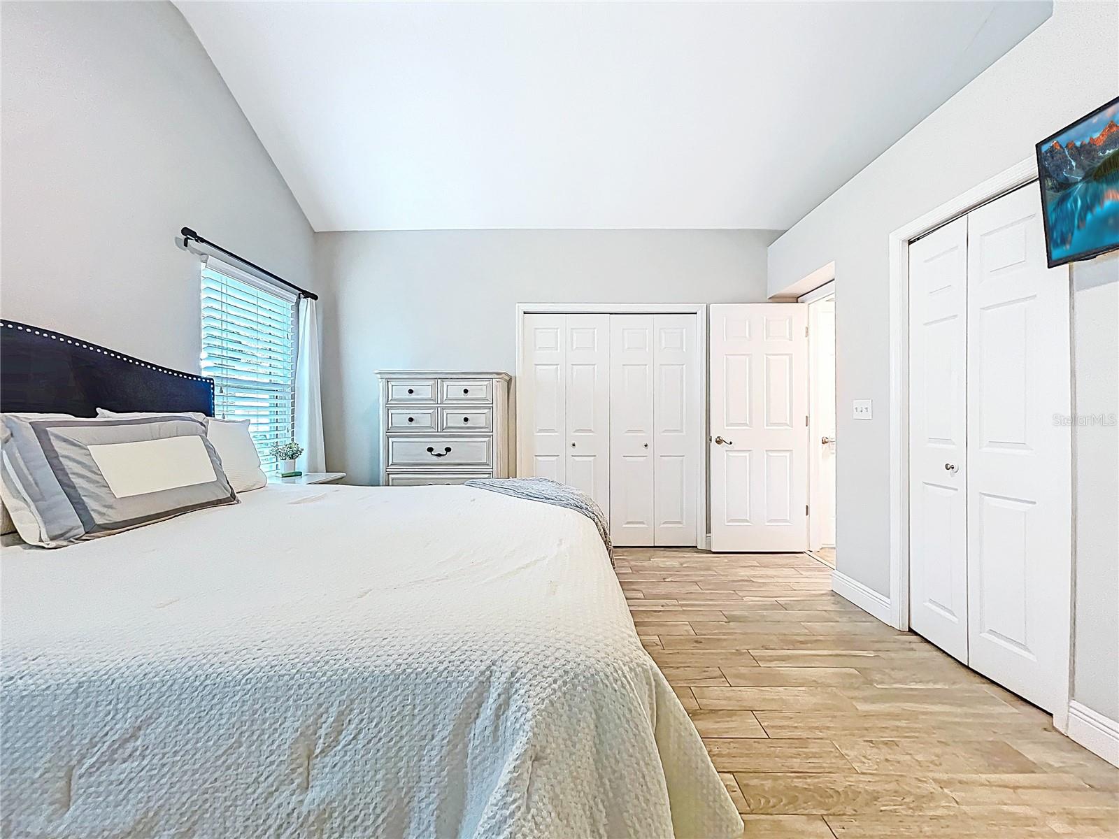 Spacious and inviting with vaulted ceilings, rich wood-look tile flooring, and soft natural light pouring through the side window. Double closets and neutral tones add both function and tranquility.