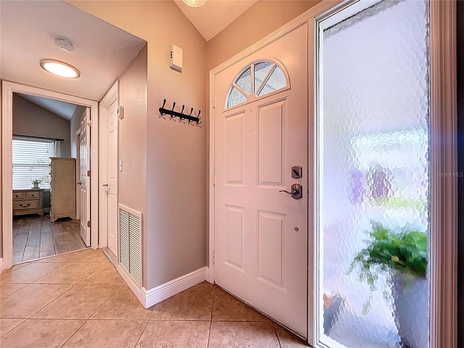 Welcoming entryway with neutral tile flooring, a decorative glass sidelight, and a convenient wall-mounted coat rack, setting the tone for the home’s clean and inviting style.