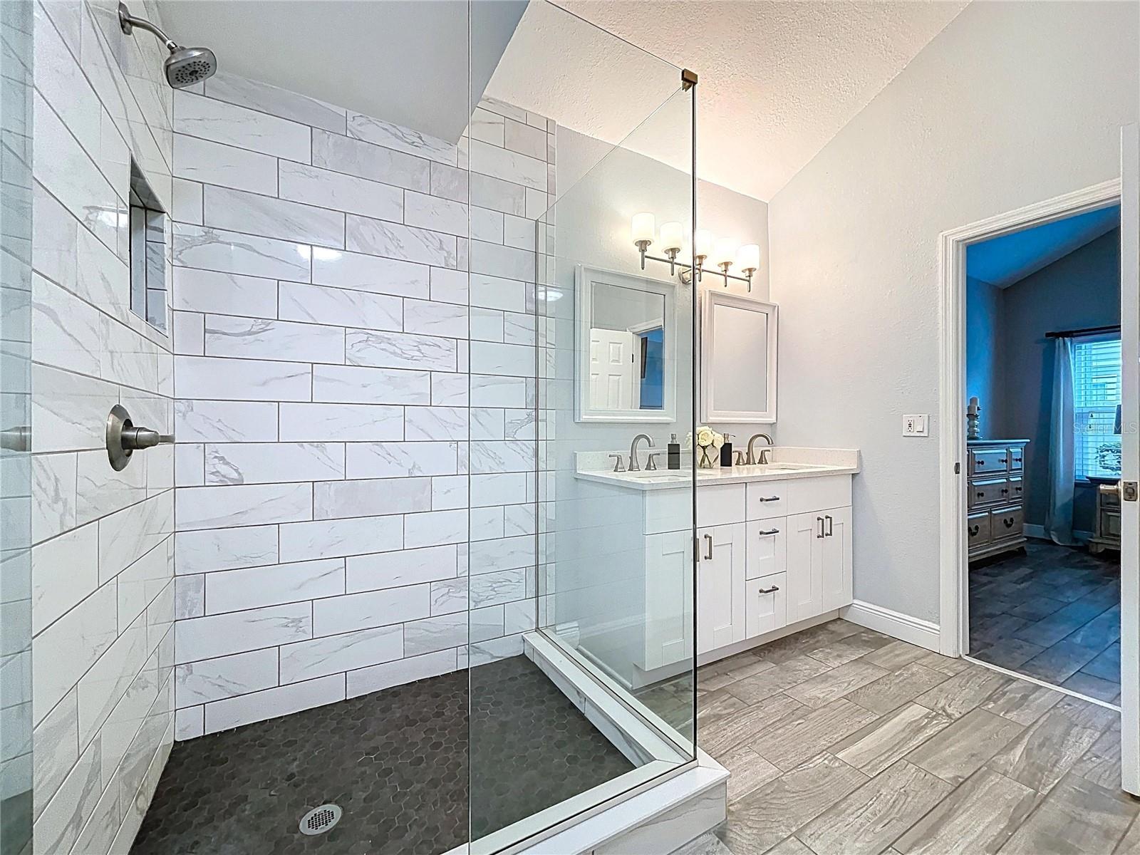 Step into a luxurious bathroom retreat with a glass-enclosed walk-in shower, elegant tilework, and dual vanity setup.