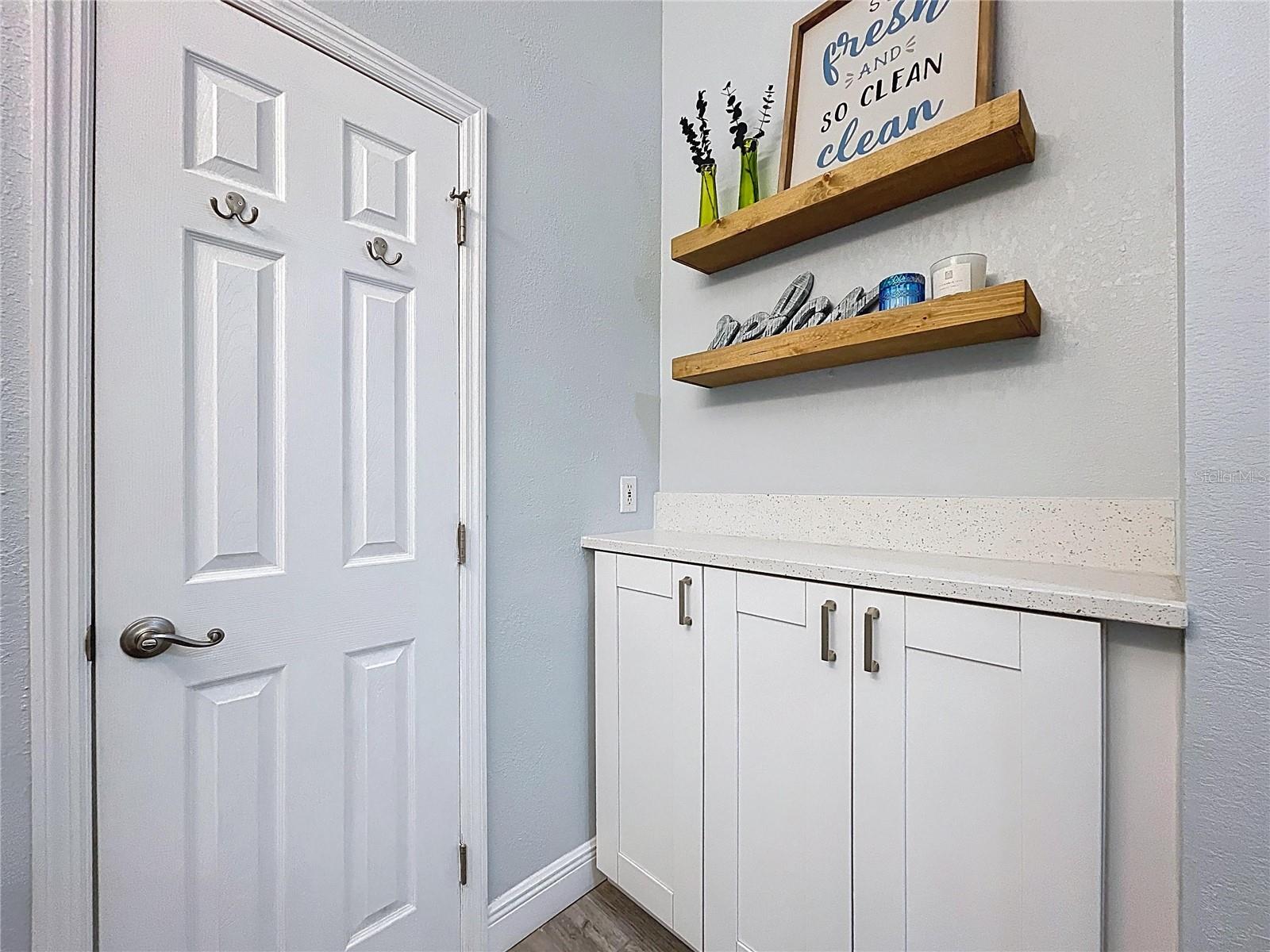 Tucked in the owners' bathroom, this custom storage zone features stylish cabinetry, open wood shelving, and a quartz folding surface—perfect for everyday organization.