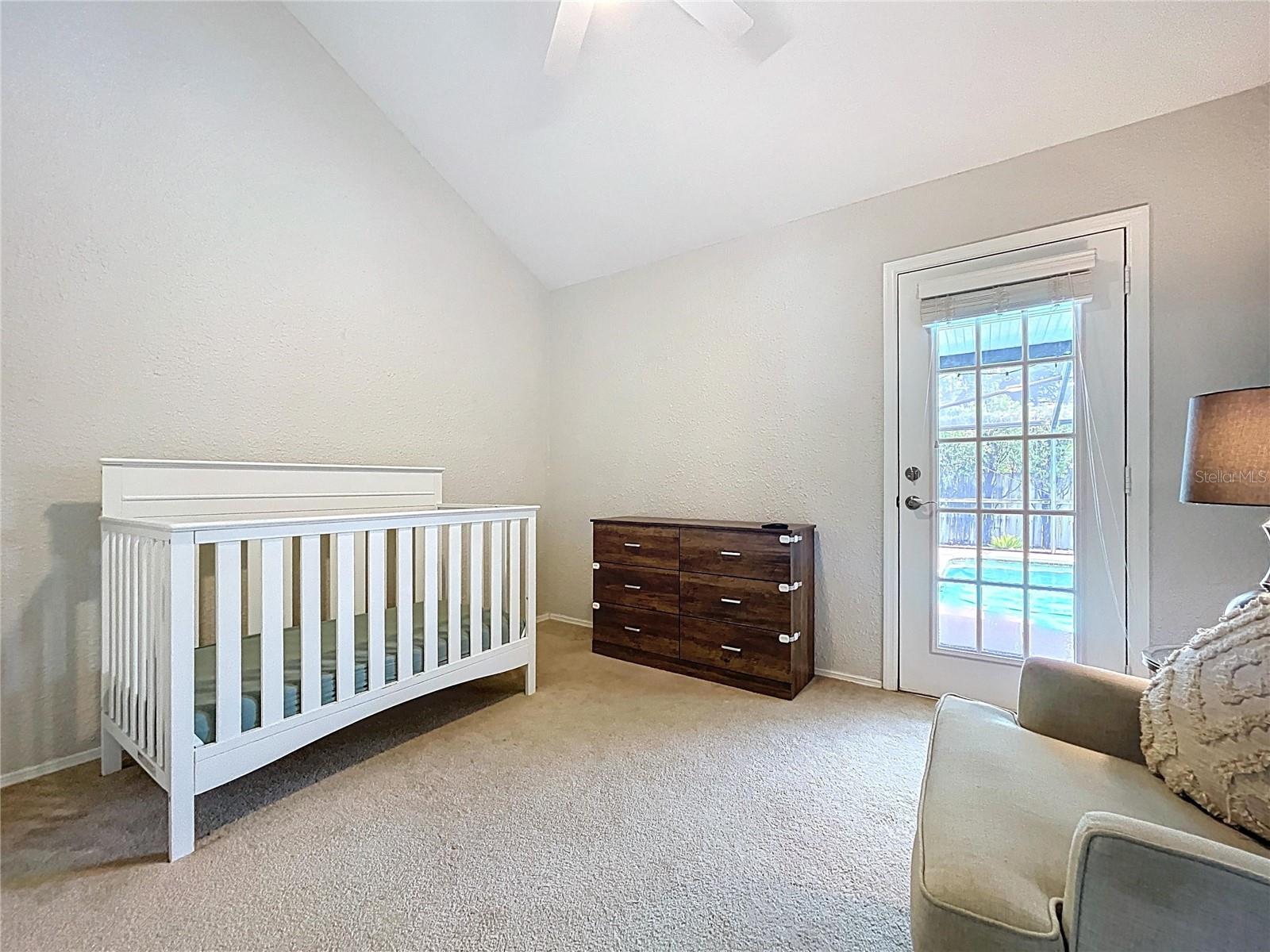 Versatile third bedroom currently used as a nursery, offering vaulted ceilings, neutral carpeting, and private access to the screened lanai and pool.
