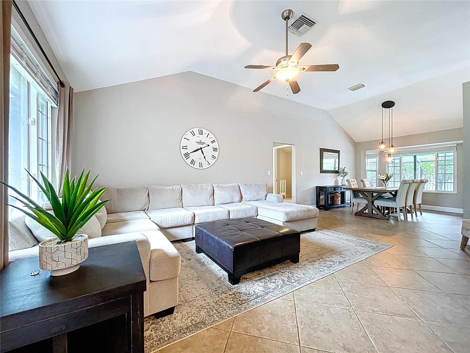 Spacious living area with vaulted ceilings, tile floors, and abundant natural light from a large front-facing window. Ideal for relaxing or entertaining.