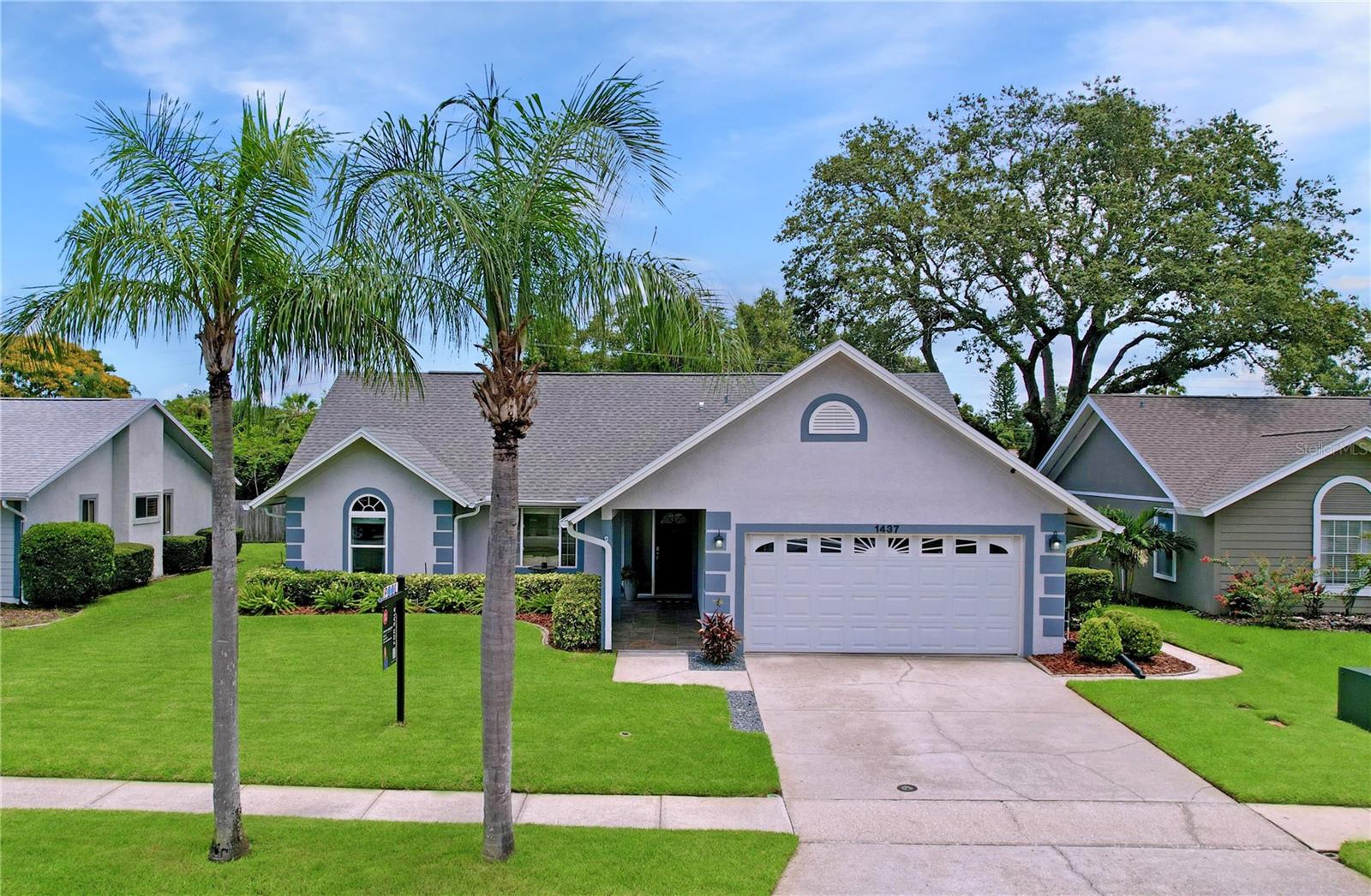 Manicured landscaping, mature palm trees, and a fresh exterior paint scheme create a picture-perfect presence on a quiet, tree-lined street.