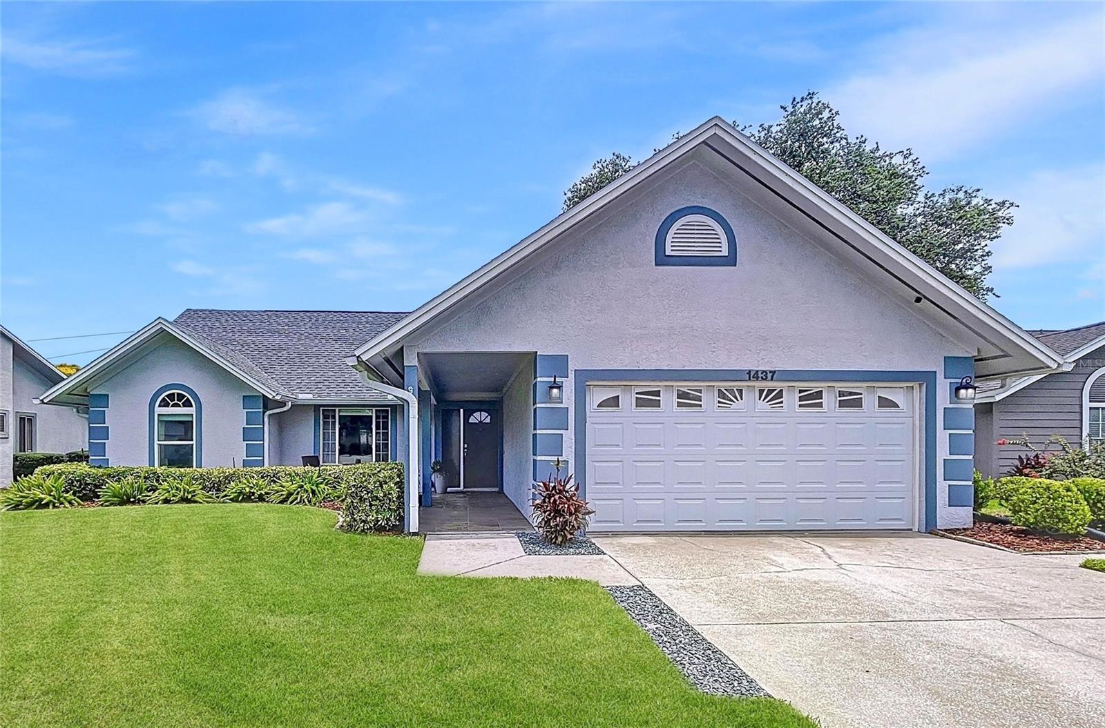The home’s classic architecture and coastal blue accents offer timeless charm, complemented by neat hedging and a clean driveway approach.
