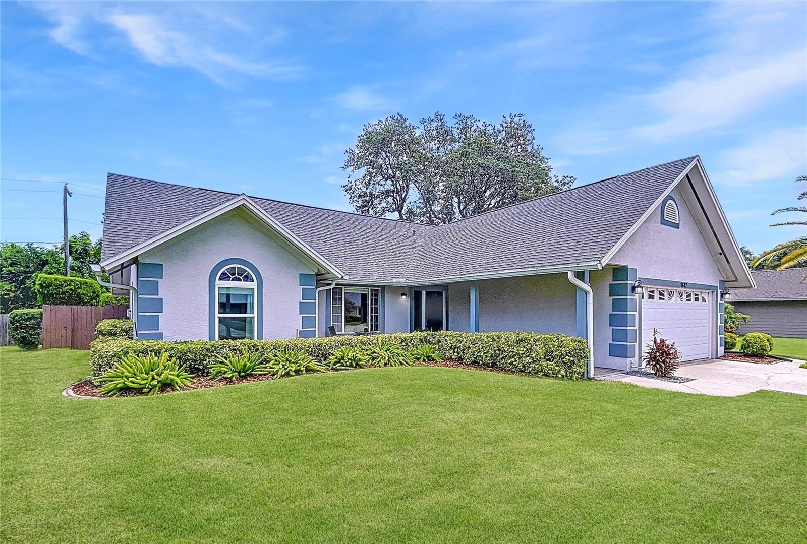A sweeping corner perspective highlights lush landscaping, a tidy lawn, and the home’s elegant symmetry.
