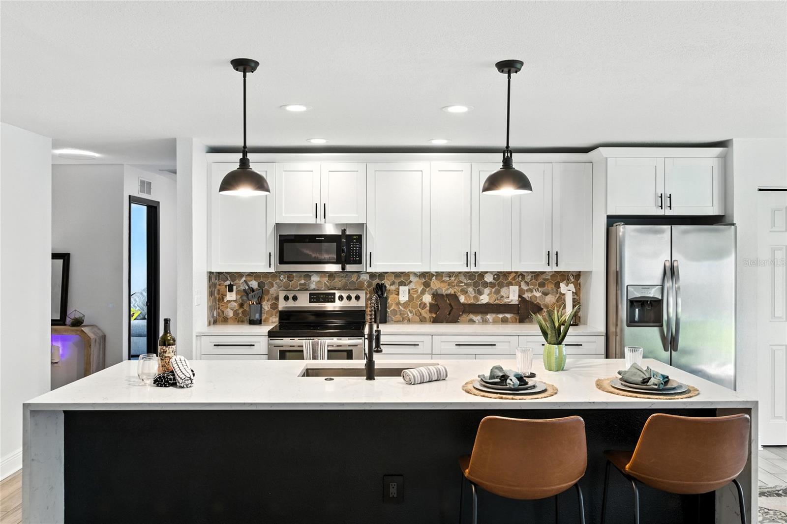 Bright white cabinetry with modern hardware pairs perfectly with warm earth-toned backsplash and stainless steel appliances, while the oversized island with deep basin sink anchors the space for both function and entertaining