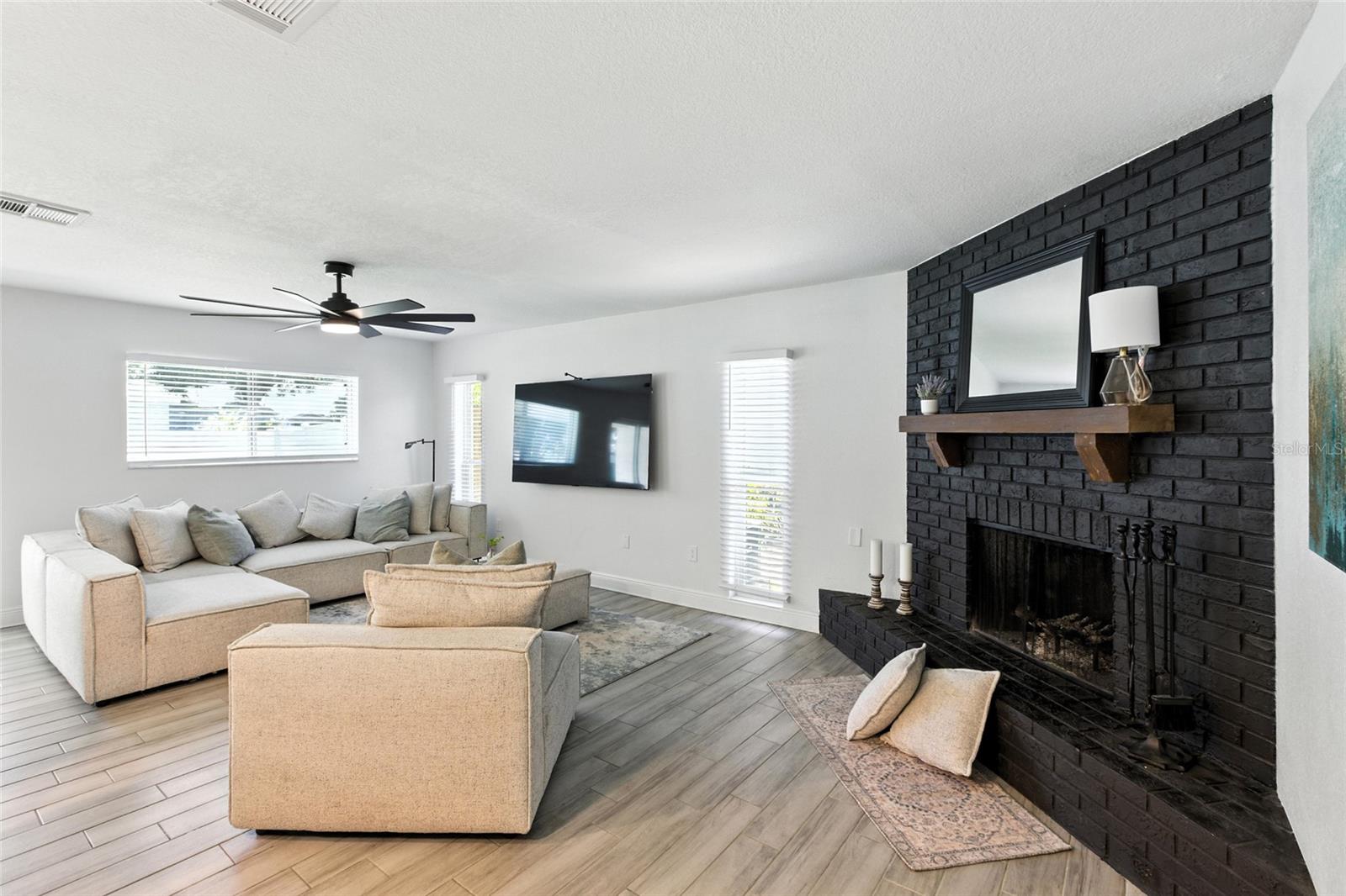 Spacious and inviting living room featuring a true wood-burning fireplace, dramatic black brick surround, and enough space for your biggest sectional and then some