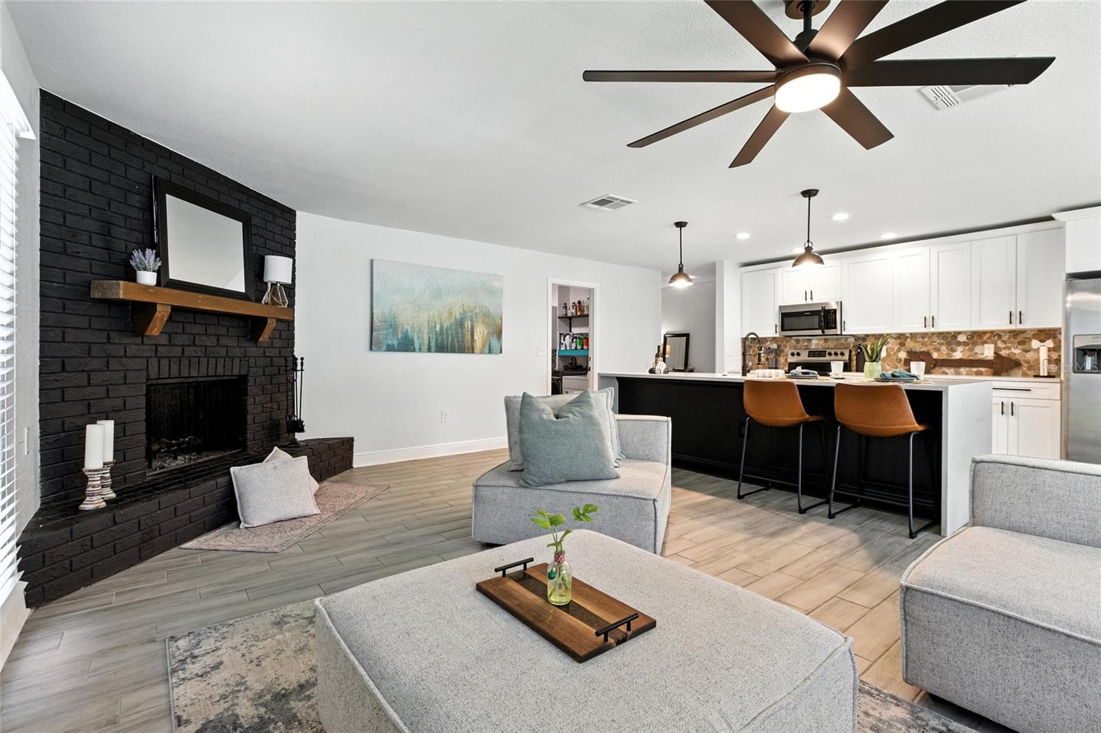 Spacious and inviting, this open-concept living area is ideal for entertaining—anchored by a bold black brick fireplace and oversized ceiling fan for added style and comfort.