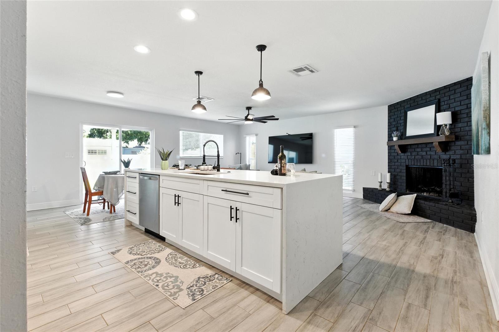 Kitchen, dining, and living all flow together in this bright, open concept space—anchored by that stunning black brick fireplace for a cozy yet modern touch.