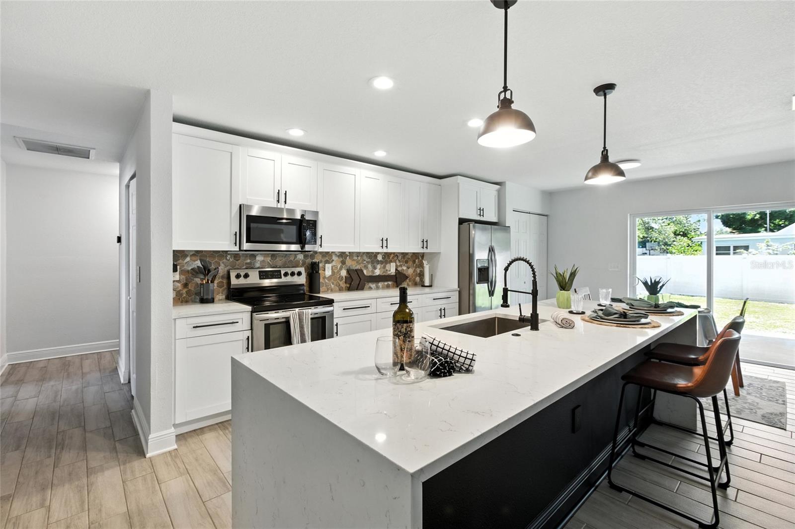 Generous cabinet storage and expansive prep space define this kitchen, featuring a striking waterfall-edge quartz island, full pantry, and modern stainless steel appliances. The sleek tile backsplash adds just the right texture and tone.