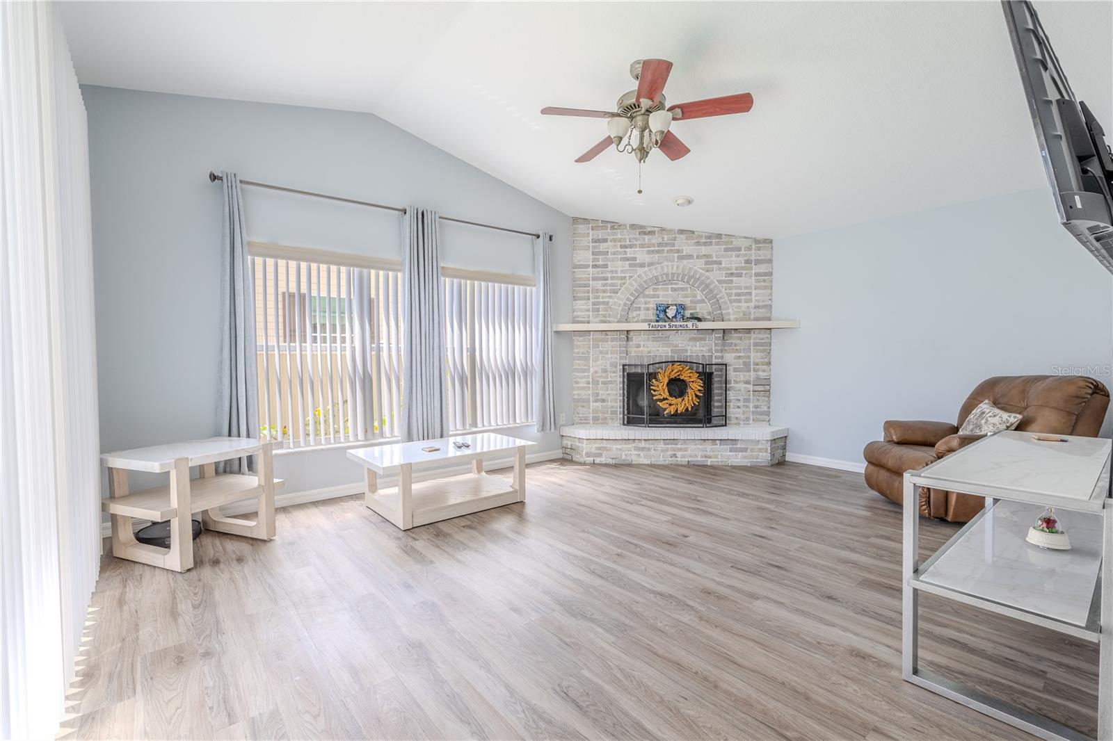 Just off the kitchen is the inviting family room—open and airy with vinyl flooring, a neutral palette, vaulted ceilings, and a wood-burning fireplace with brick surround and hearth.