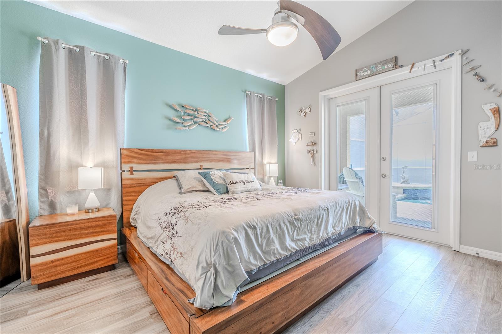 The primary bedroom features high ceilings, vinyl flooring, a modern ceiling fan, and French doors that open to the lanai and pool.