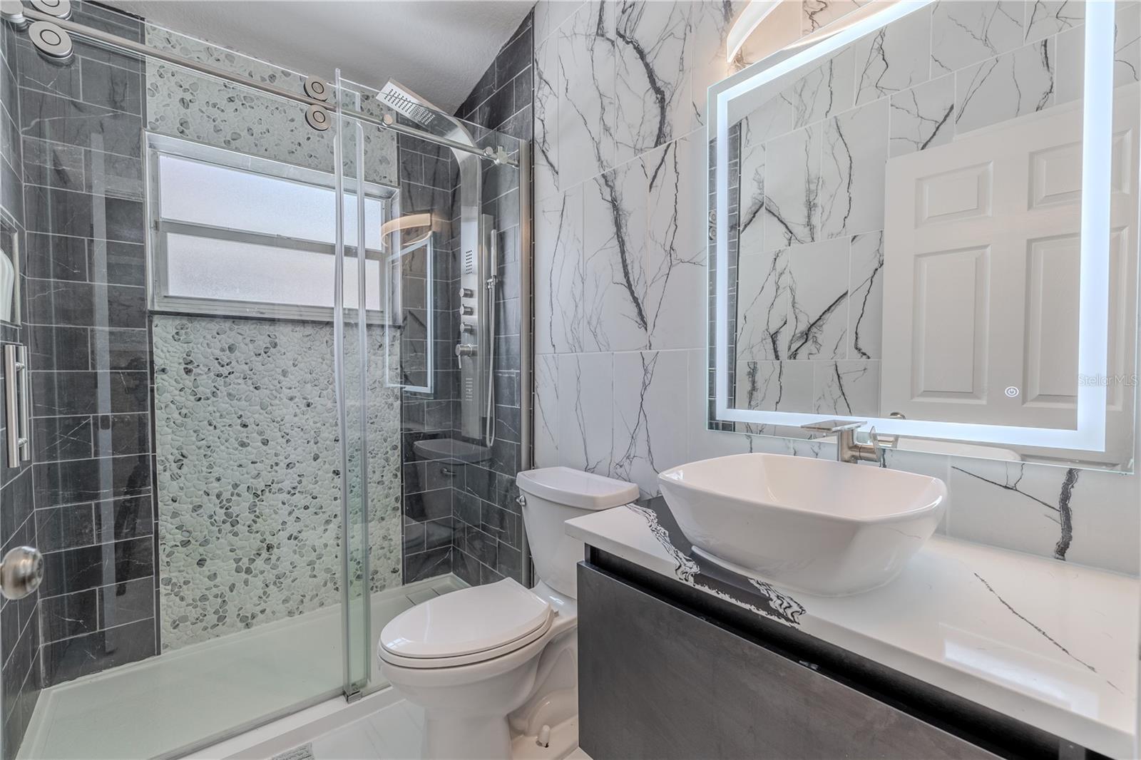 Bathroom 2 is a showstopper—fully updated with a spa-inspired design that includes a river rock-accented walk-in shower, rainfall shower tower, charcoal tile, a vessel sink, quartz vanity, and an LED backlit mirror for that perfect glow.