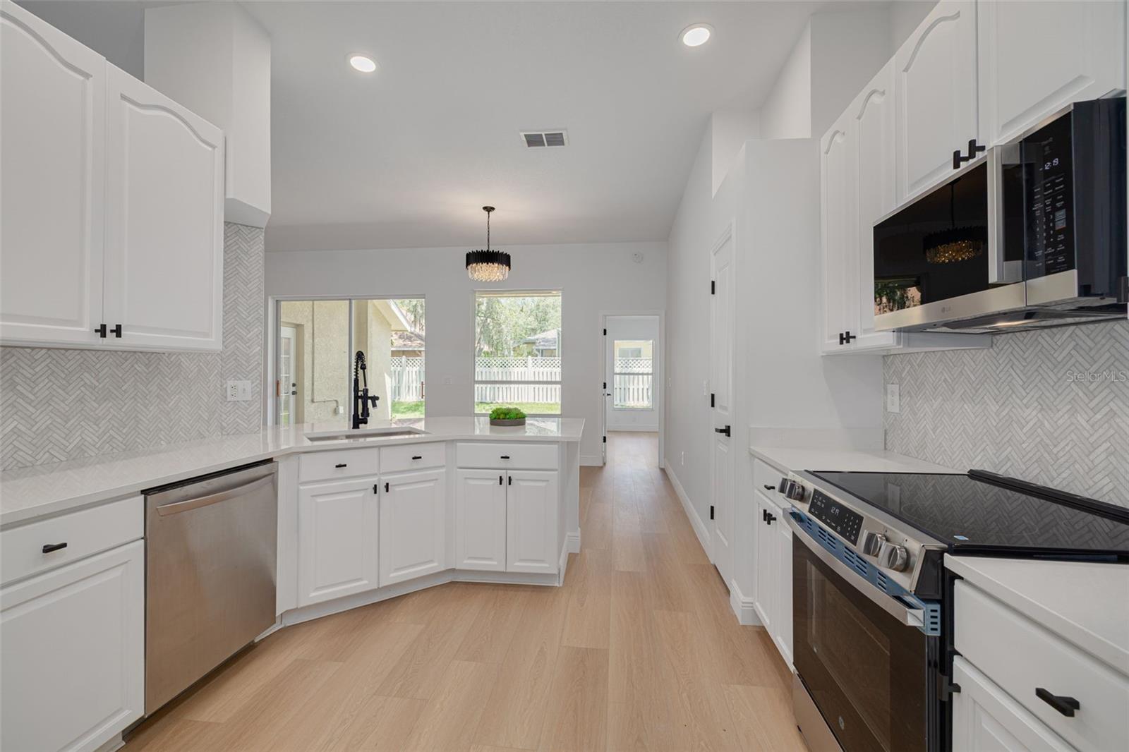 This galley kitchen showcases the perfect balance of style and function with stunning herringbone tile backsplash and elegant chandelier lighting. The abundant cabinetry and new stainless steel appliances provide everything a home chef could desire.