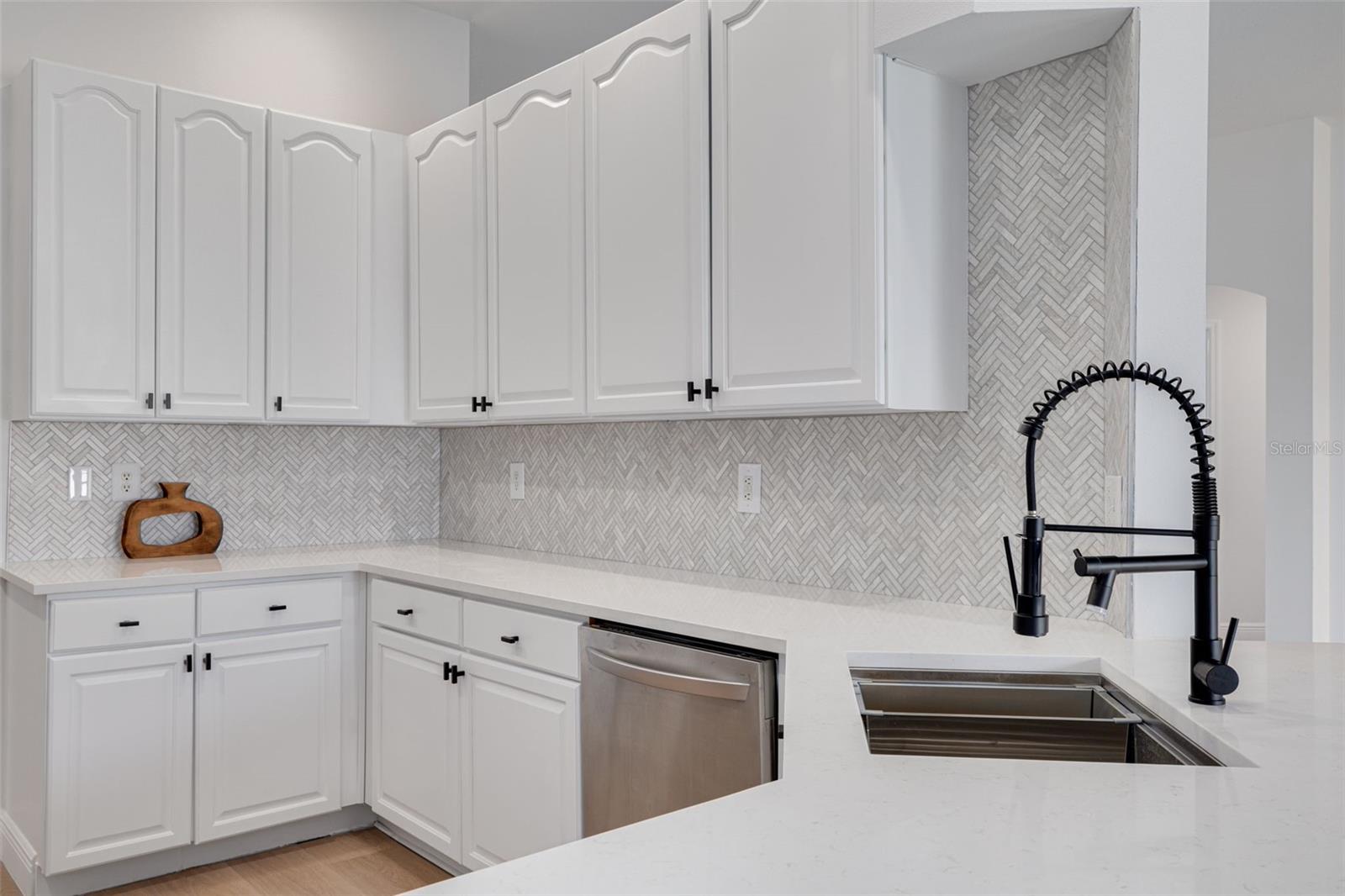 This corner view highlights the attention to detail in every aspect of the kitchen renovation including the gorgeous herringbone backsplash and professional-grade faucet. The abundant storage and pristine quartz countertops make this kitchen both beautiful and highly functional.