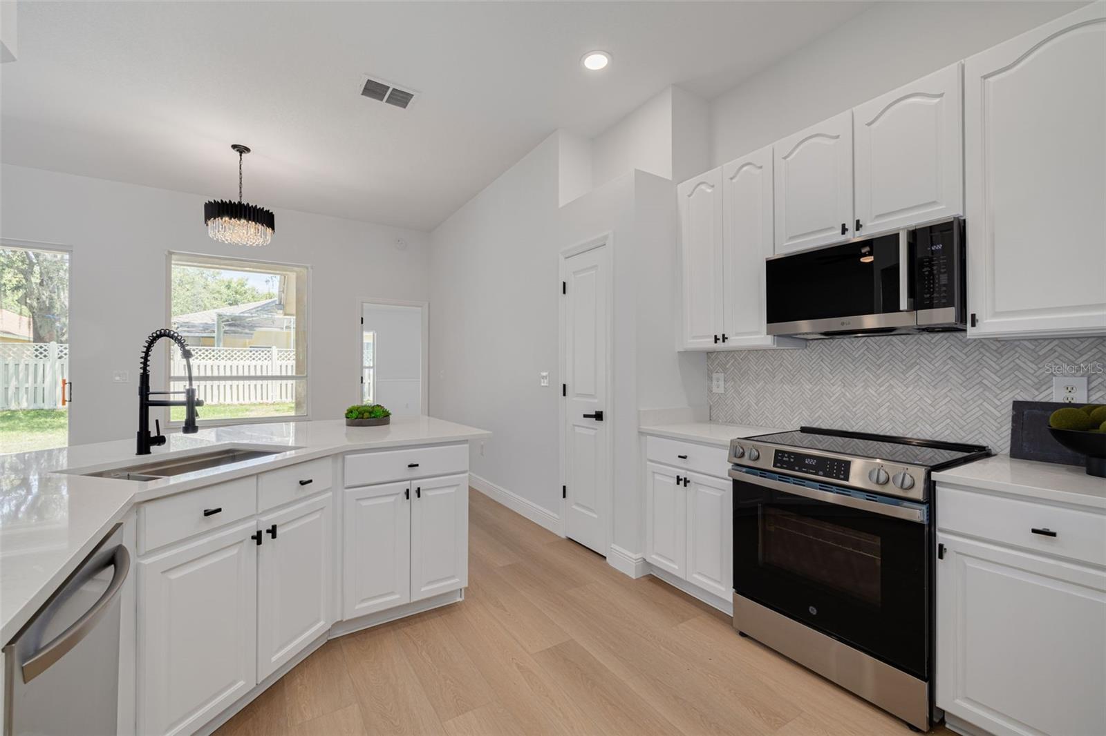 Admire the seamless integration of new stainless steel appliances including microwave and range with the beautiful white cabinetry. The herringbone backsplash and quartz countertops create a luxurious yet practical workspace for daily cooking and entertaining.