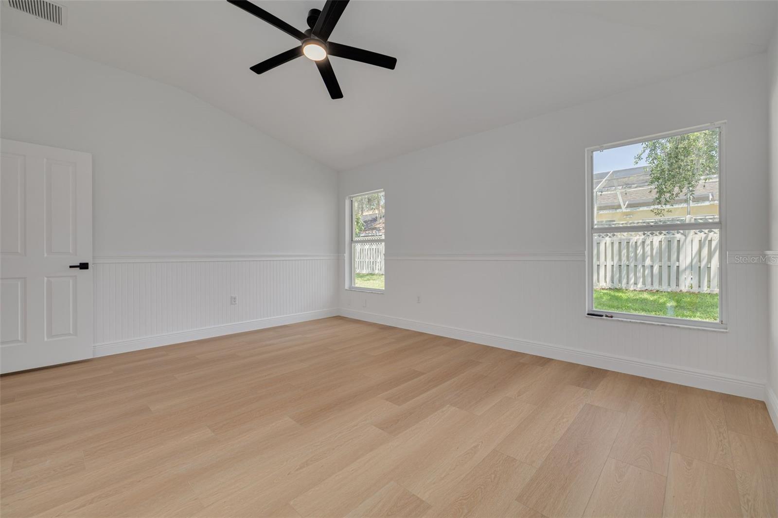 This charming bedroom showcases elegant wainscoting details and custom molding that add architectural interest and sophistication. The new ceiling fan and quality flooring continue the premium finishes found throughout this beautifully renovated home.