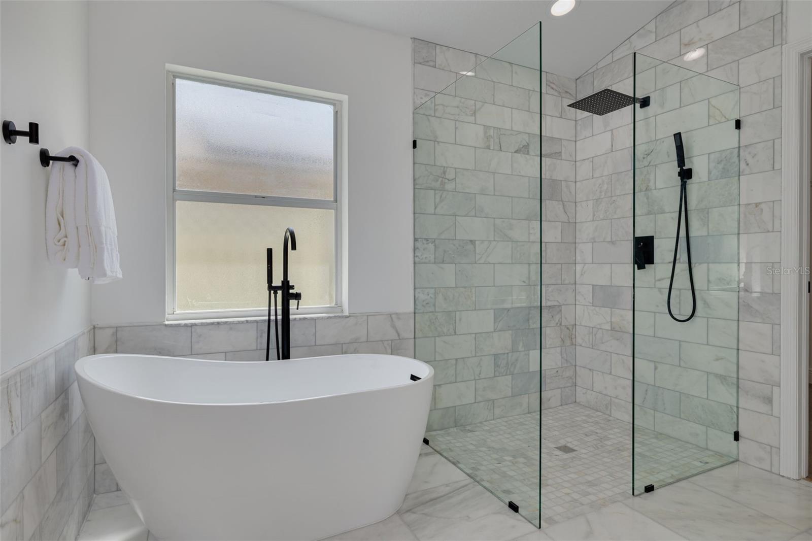 Indulge in the ultimate spa experience with this stunning master bathroom featuring a freestanding soaking tub and frameless glass shower with marble surround. The modern black fixtures and premium finishes create a luxurious escape that rivals any high-end resort.