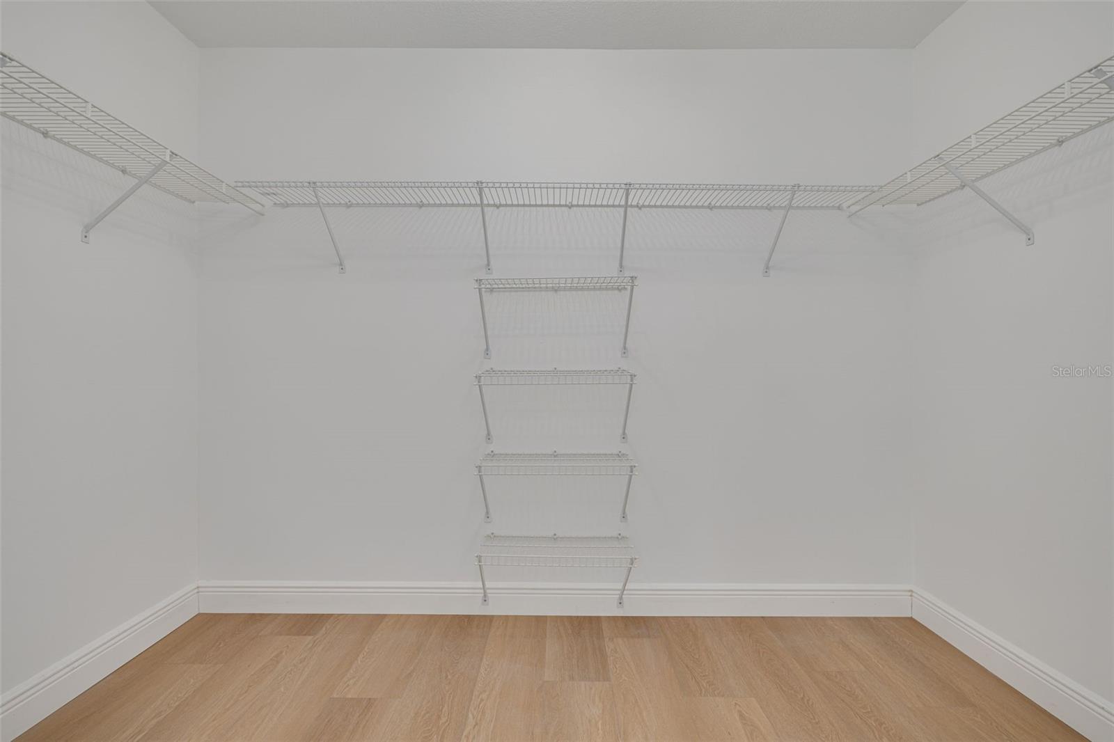 This spacious walk-in closet features professionally installed wire shelving systems that maximize storage and organization for your entire wardrobe. The luxury vinyl plank flooring and thoughtful design make getting dressed each day a pleasure.