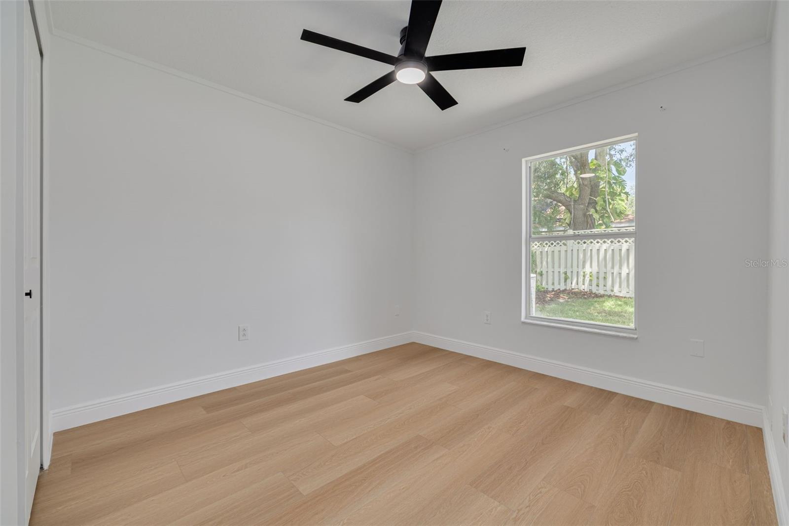 This bright and cheerful bedroom features a large window that overlooks the private backyard and lush landscaping beyond. The new ceiling fan with lighting and quality flooring make this space perfect for children, guests, or a home office.