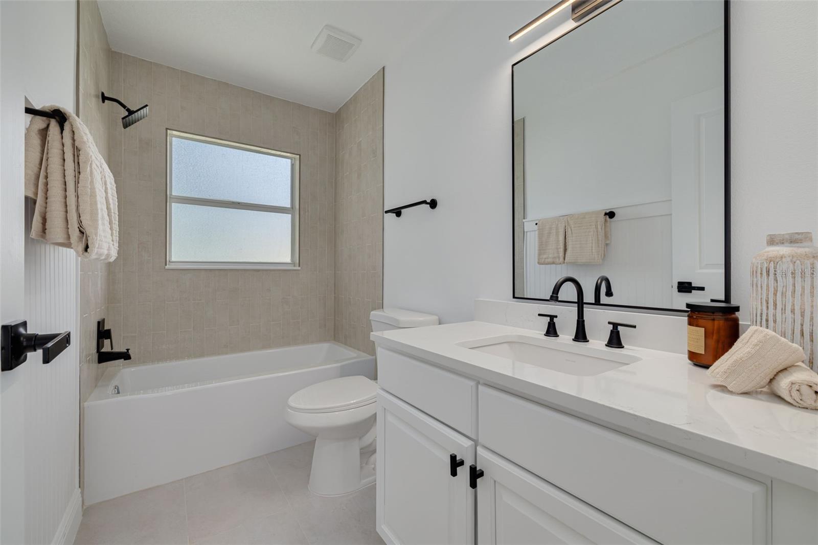 This completely renovated guest bathroom features vertical running bond tile and modern quartz countertops for a timeless yet contemporary look. The elegant black fixtures and professional lighting create a spa-like experience for family and visitors.
