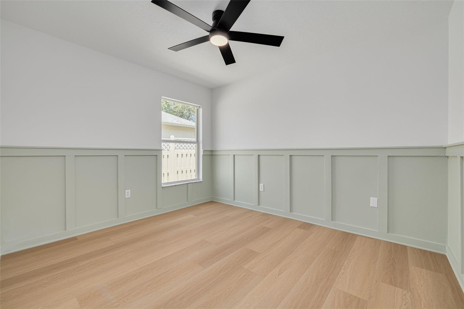 This stunning bedroom features custom wainscoting details that showcase the quality craftsmanship throughout the home. The elegant sage green accent and modern ceiling fan create a sophisticated space that feels both cozy and refined.