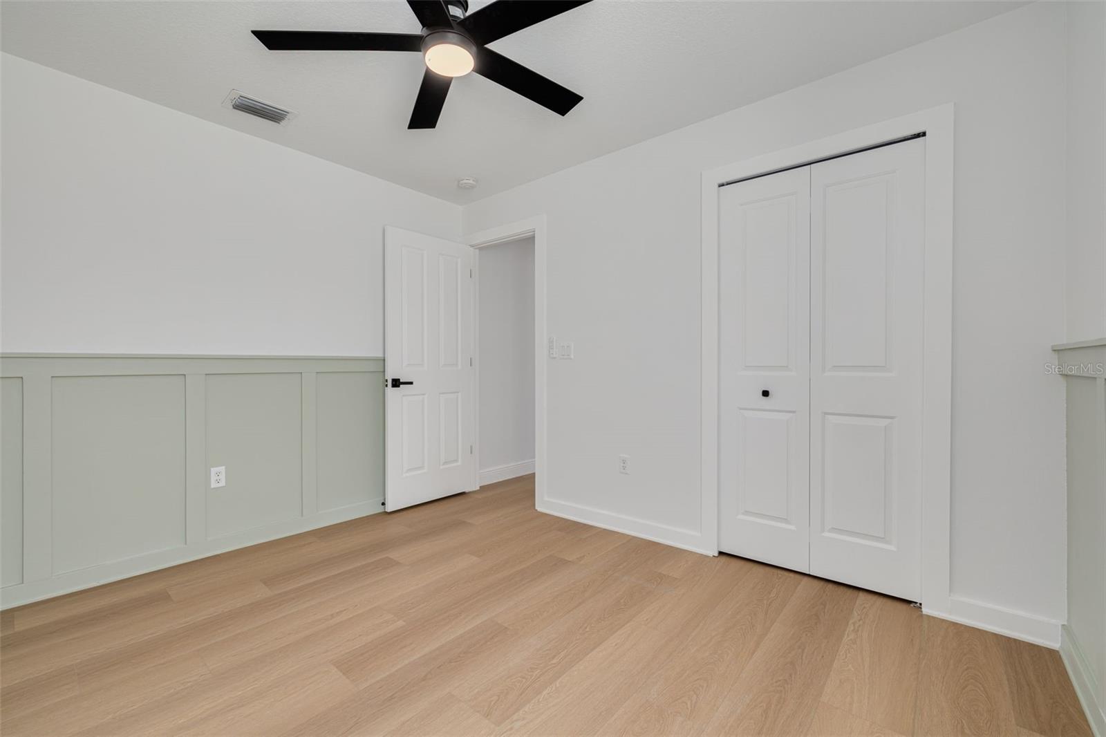 This elegant bedroom showcases beautiful custom wainscoting in a soft sage green that adds character and sophistication to the space. The new ceiling fan and luxury vinyl plank flooring create a serene retreat with timeless appeal.