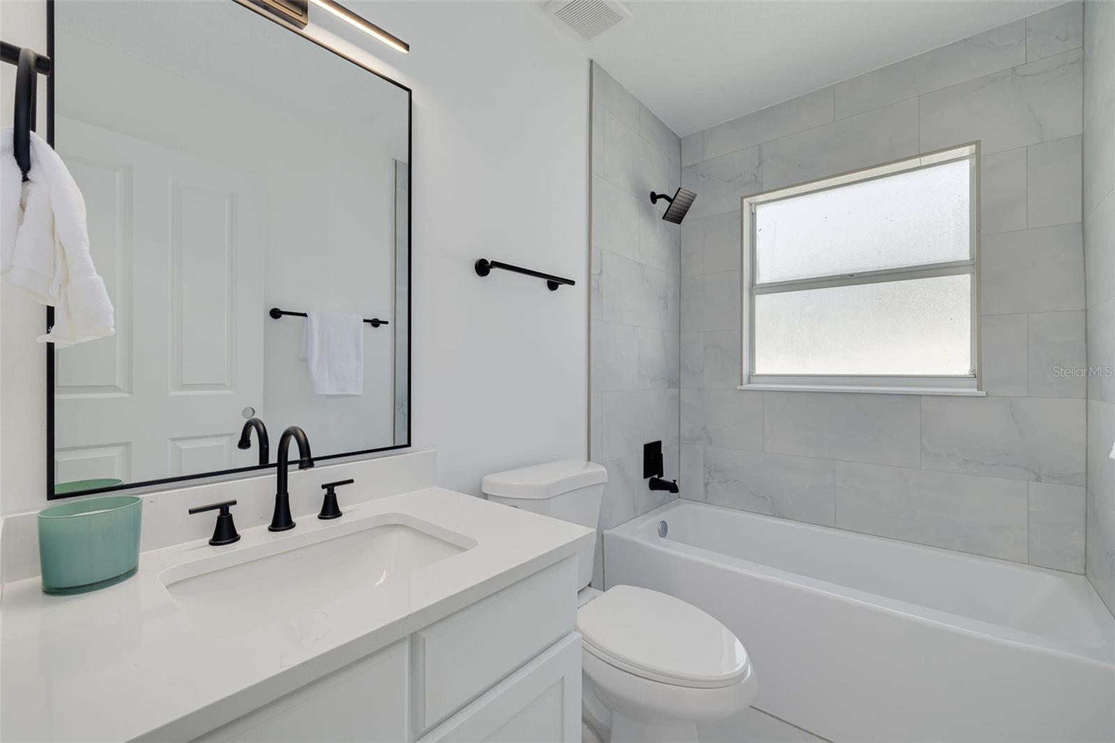 This beautifully renovated guest bathroom showcases stunning quartz countertops and modern black fixtures that complement the home's sophisticated design. The elegant lighting and premium tile work create a welcoming space for family and guests.