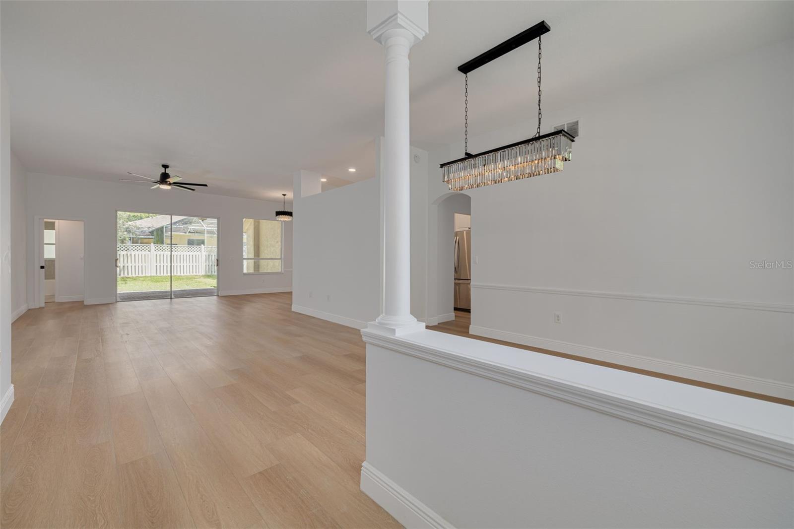 Experience the wow factor of this open-concept great room featuring a show-stopping crystal chandelier and soaring ceilings with elegant columns. The beautiful luxury vinyl plank flooring flows seamlessly throughout, while French doors lead to additional living spaces.