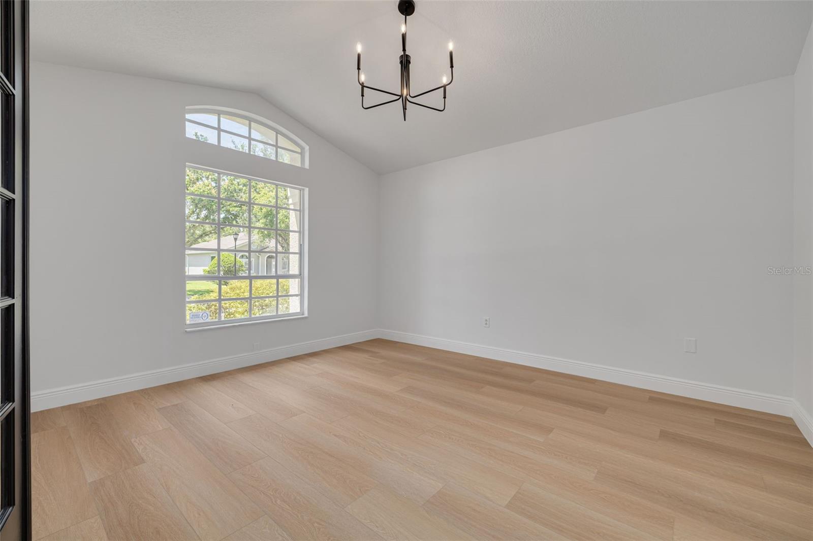 This bright and airy room features a stunning arched window that frames views of the neighborhood's mature trees and landscaping. The sophisticated lighting and quality flooring make this space perfect for work, study, or quiet relaxation.