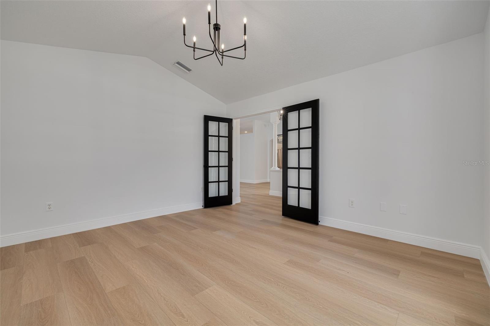 Step into this versatile space that can serve as a formal dining room, home office, or additional bedroom to suit your lifestyle needs. The dramatic black French doors and modern chandelier create an elegant atmosphere while the luxury vinyl plank flooring adds warmth.