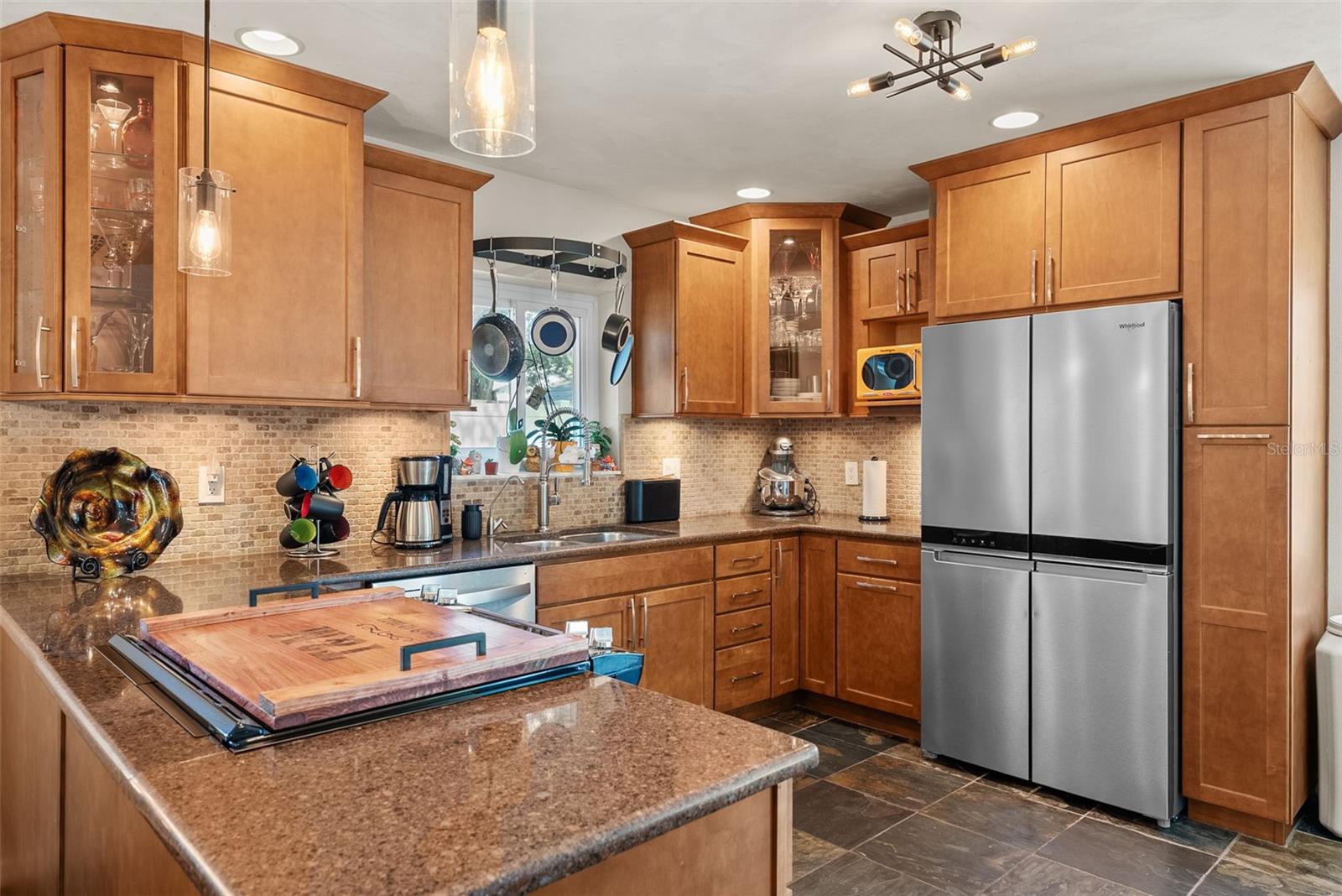 Kitchen - new appliances 2025 . Granite countertops, hardwood, cabinetry with glass and layers and beautiful backsplash featuring a window for plenty of natural light.